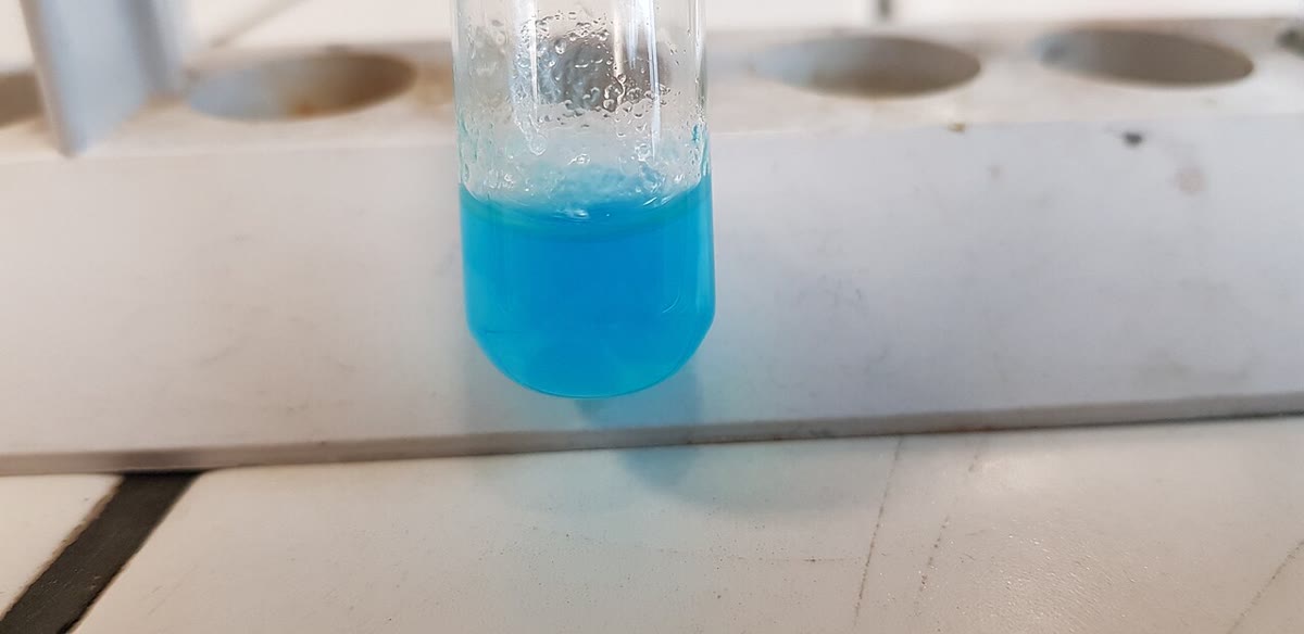Links: een suspensie van lichtblauw koper(II)hydroxide (foto Alvy16, CC BY 4.0). Rechts: met meer ammoniak lost de vaste stof op tot het diepblauwe tetraamminekoper(II)ion; onderin de buis ligt nog wat onopgelost hydroxide (foto Chemicalinterest, publiek domein). Beide Wikimedia Commons.