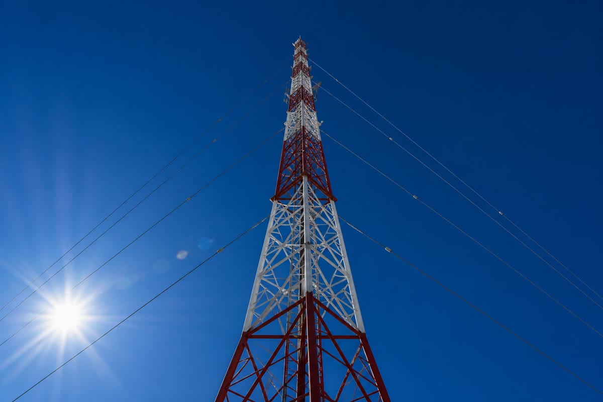 Een zendmast onder een blauwe hemel: een verticale dipool van tientallen meters die naar de horizon straalt, en daarboven de hemel die door miljarden moleculaire dipolen wordt verlicht die de zon opnieuw uitstralen.
