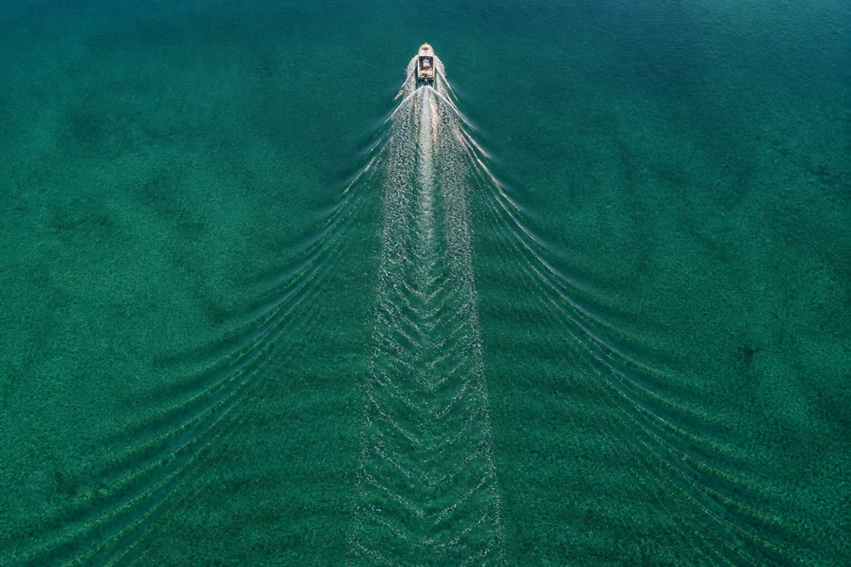 The wake of a motorboat on a calm lake: the feathered pattern stays inside a wedge of fixed angle because the energy of each water wave travels at half the speed of its crests — dispersion made visible.