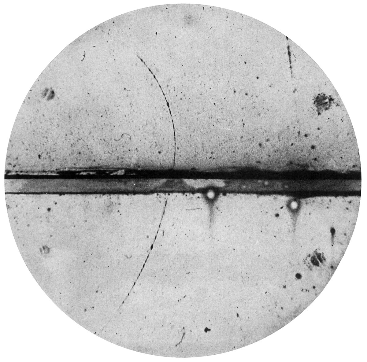 El descubrimiento de la antimateria (Carl D. Anderson, 1932, dominio público): un único positrón que asciende atravesando la placa de plomo de la cámara de niebla, curvándose al revés que un electrón y demasiado cerrado para ser un protón — la contabilidad de E = mc2 sorprendida marchando al revés.